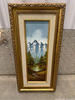 Full view of the vertically oriented framed oil painting showing mountains, trees, and river in a gold ornate frame.