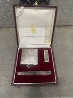 Closed display case with three silver items arranged inside, lined with red velvet and white satin interior.