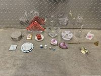 Wide view of assorted vintage trinkets including glass bowls, porcelain dishes, small boxes, salt and pepper shakers, and decorative figurines arranged on metallic surface.