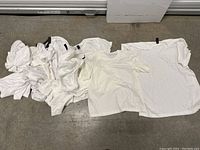 Photo showing approximately 14 white shirts in various sizes and styles, including short-sleeve and long-sleeve.