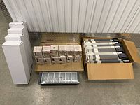 Full view of lot showing three main item groups: stacked white vertical wine boxes on the left, multiple boxed display stands on the right, and clear plastic trays in front.