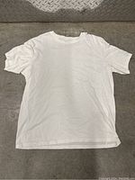 Full front view of the white crew neck T-shirt laid flat on a concrete surface, showing condition and size.