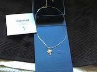 Full view of gold chain necklace with pendant on a blue cloth.