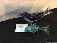 Both dolphin figurines placed together on a black surface showing size and condition, including the small crack on the blue dolphin's nose.