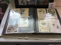 Photo of an open photo album page with vintage postcards featuring floral, architectural, and holiday themes