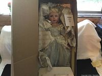 Porcelain Cinderella doll dressed in blue gown inside open box with tissue paper padding.