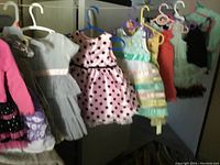 Image showing various baby and toddler girl dresses hanging on hangers including polka dots, pleats, floral, and striped patterns