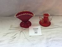 Two cranberry glass pieces including a pedestal bowl and a candle holder with ruffled clear edges and gold rims.