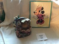 Framed 1987 Minnie Mouse illustration in turquoise-green frame standing upright next to dolphin statue.