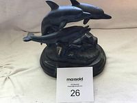 Side view of dark dolphin statue showing three dolphins arranged on a rounded base with textured surface