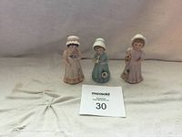 Three Enesco 1986 figurines, young girls in bonnets holding musical instruments, placed on a light cloth background.
