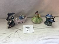 Overview of four porcelain figurines including Chorley dog, two dolphin figurines, and china doll.
