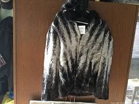Full view of the faux fox fur coat hanging on a hanger, showing black and white striped pattern and hood.