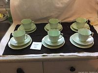 Front view of tea set with six cups, saucers, and plates displayed on a black cloth.