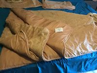 Golden king comforter partially folded showing textured and smooth sides with rope trim edge on blue background.