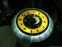 Clock face front showing rotating moon and stars design, yellow and black dial with bold numbers 1-12, illuminated neon rim glowing white/blue.