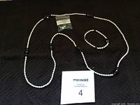 Photo shows a long necklace, a bracelet, and earrings all featuring white freshwater pearls and black onyx beads, arranged around a MaxSold card with lot number 4.