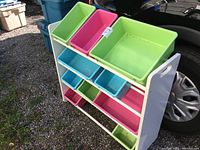 Photo showing front angle of white storage rack with multiple colored plastic storage bins in outdoor setting.