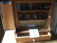 Wooden display case with glass front door containing multiple Red Rose Tea ceramic figurines on two shelves.