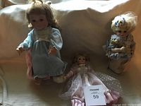 Three vintage dolls on a beige couch, showing various dresses and sizes.