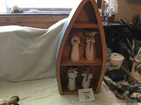 Photo showing wooden boat-shaped shelf with four Willow Tree angel statues arranged on two shelves.