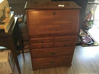 Front view of wooden writing desk with fold-down front panel and three exterior drawers.