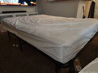 Photo showing queen mattress covered with protective plastic liner on fold away metal frame