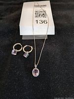 Photo showing the silver necklace with oval amethyst pendant and matching silver hoop earrings with amethyst drops.