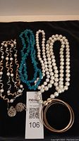 Overview of all items in the lot including pearl necklaces, turquoise necklace, gold-tone bangles, and earrings displayed on black cloth