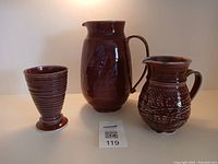 Photo showing all three burgundy pottery pieces - large jug, smaller jug, and vase with seller's lot number card in front