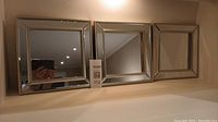Photo shows three square decorative mirrors, each 10 inches square, with metallic beveled frames. Positioned side by side on a flat surface against a wall. Reflections visible in mirrors.