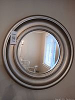 Front view of the round beveled mirror showing the champagne-colour painted frame with layered circular ridges, displayed leaning against a wall.