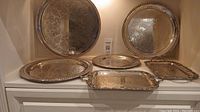 Full set of six silver plated trays including large round tray, two 12-inch trays, one 9-inch tray, and two rectangular trays with handles.