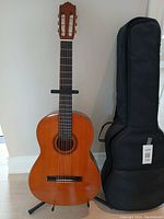 Front view of Yamaha guitar on stand with black soft-sided case beside it