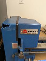 Photo showing the headstock of the lathe with the Atlas Clausing Corporation badge and visible damage (chip) on the blue metal housing.