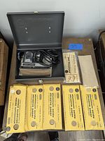 Photo showing Craftsman electric sander in metal storage box with power cord and sandpaper packages surrounding the box.