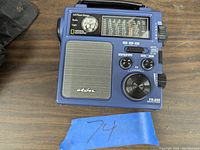 Photo showing the front of the dark blue National Geographics FR-250 emergency radio with speaker, tuning and volume knobs, battery test dial, and flashlight.