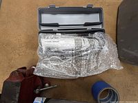 Electric carving/cutting utensil inside gray plastic carrying case wrapped in bubble wrap on workshop floor