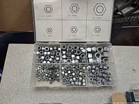 Plastic compartment box with assorted metal nuts and fasteners sorted by size.