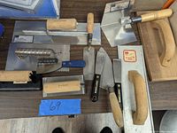 Overview of mixed lot of masonry trowels, floats, and finishing tools on a dark brown wooden surface.