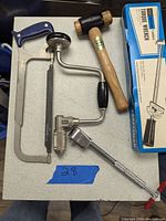 Lot contents showing hacksaw, hand crank drill, torque wrench in box, socket wrench, and mallet on a table