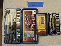 Two open metal cases showing socket sets with ratchets, screwdriver handle, sockets and extensions organized inside