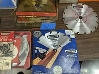 Craftsman saw blade in plastic packaging marked 10 inch cross cut plywood blade, and a silver blade outside packaging marked Craftsman Kromedge.