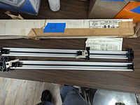 Photo showing two slide bar clamps laid on a wooden table along with the original box and instruction sheet.