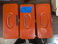 Three orange rectangular metal utility boxes with visible handles and labels
