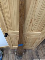 Full view of the wooden pry bar leaning against a wooden door, showing its length and wood grain.