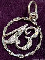Close-up photo of the 10K gold pendant showing the twisted rope circle border and number '13' design with mixed surface finishes.