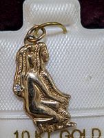 Close up of the gold pendant showing detailed side view of the woman figurine and small embedded stone