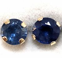Close-up image of two round blue sapphire studs in 10K gold prong setting on white background.