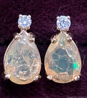 Close-up front angle of the pair of 14K gold earrings with pear-shaped opals and diamond accents on dark fabric background